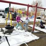 Children playing on a swing set with snow on the ground.