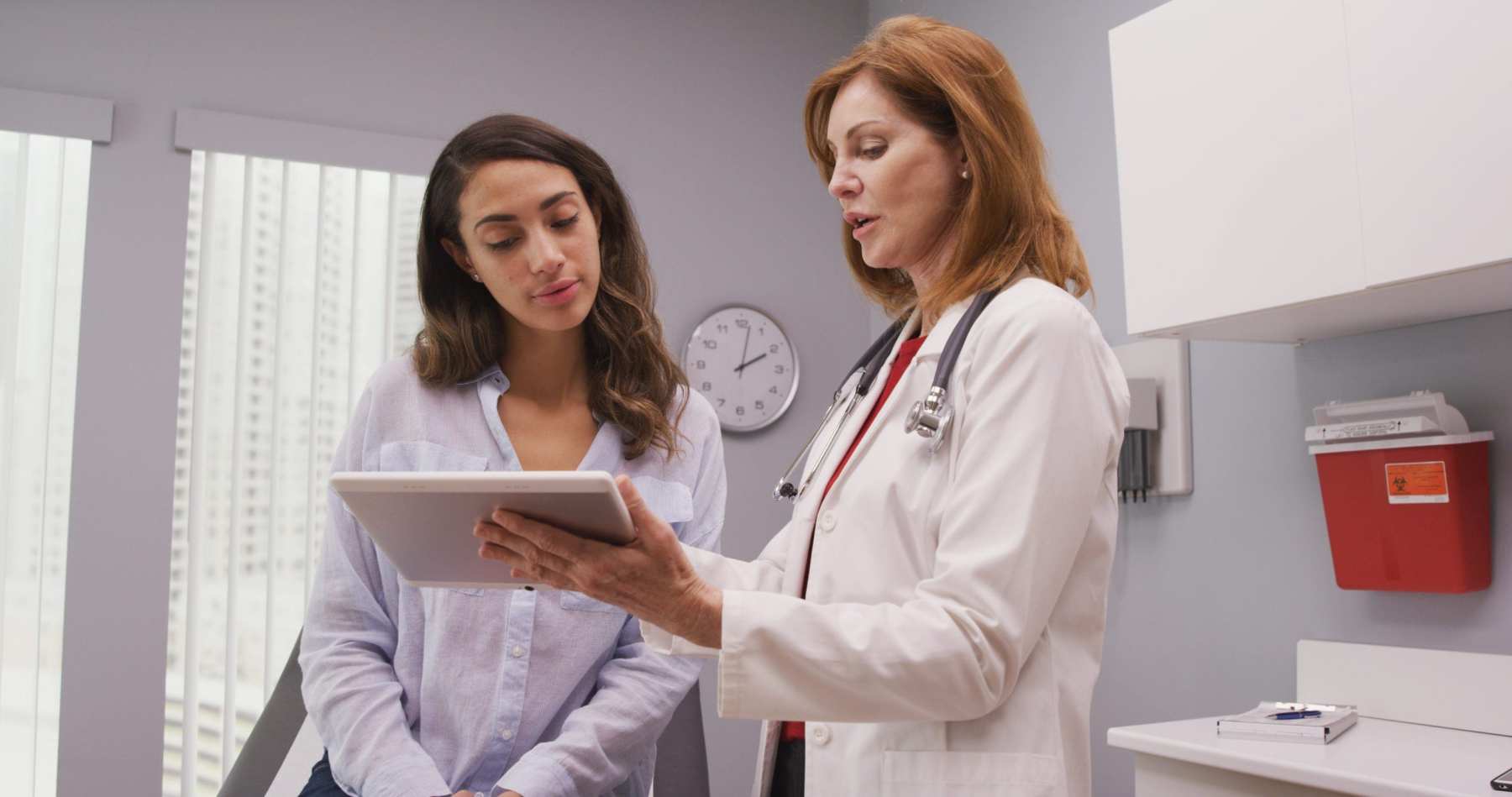 Mid aged medical doctor using portable tablet to review test results of patient.