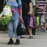 People wait in line with grocery bags.