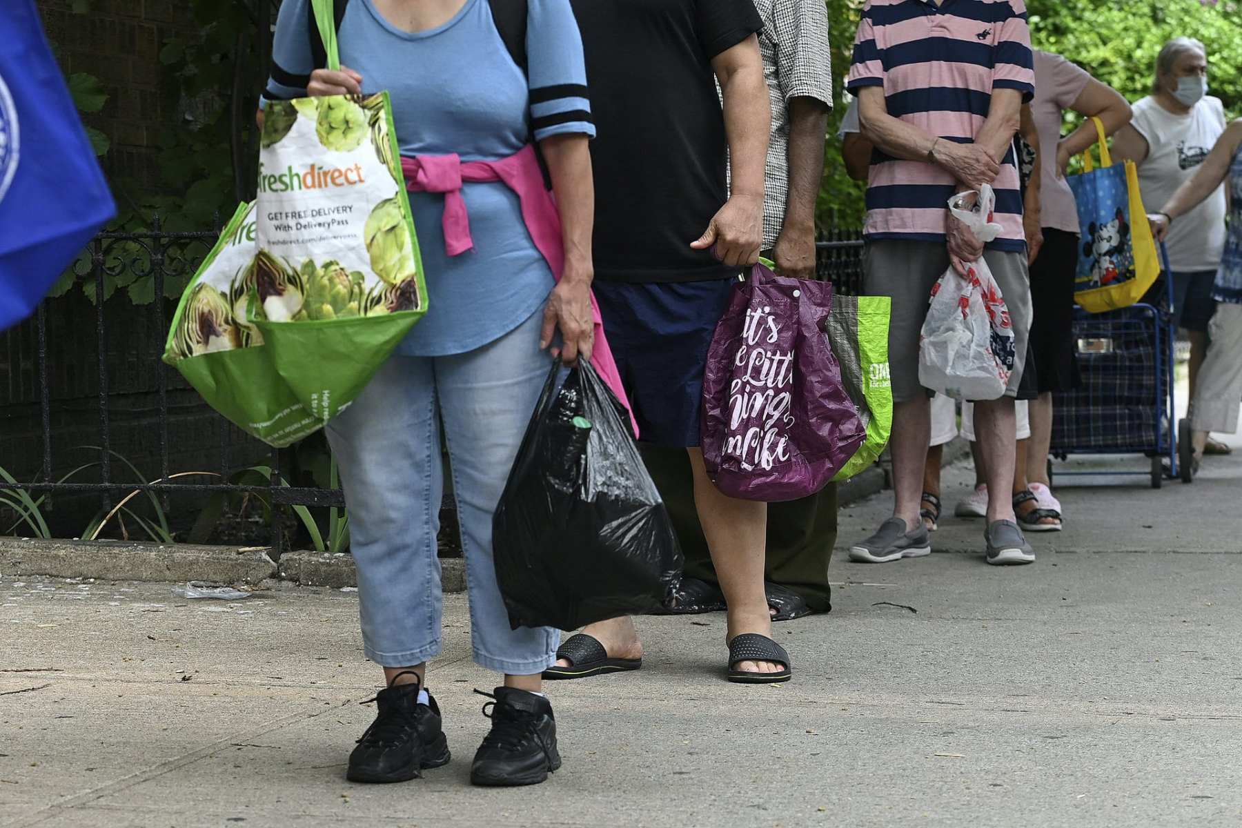 People wait in line with grocery bags.