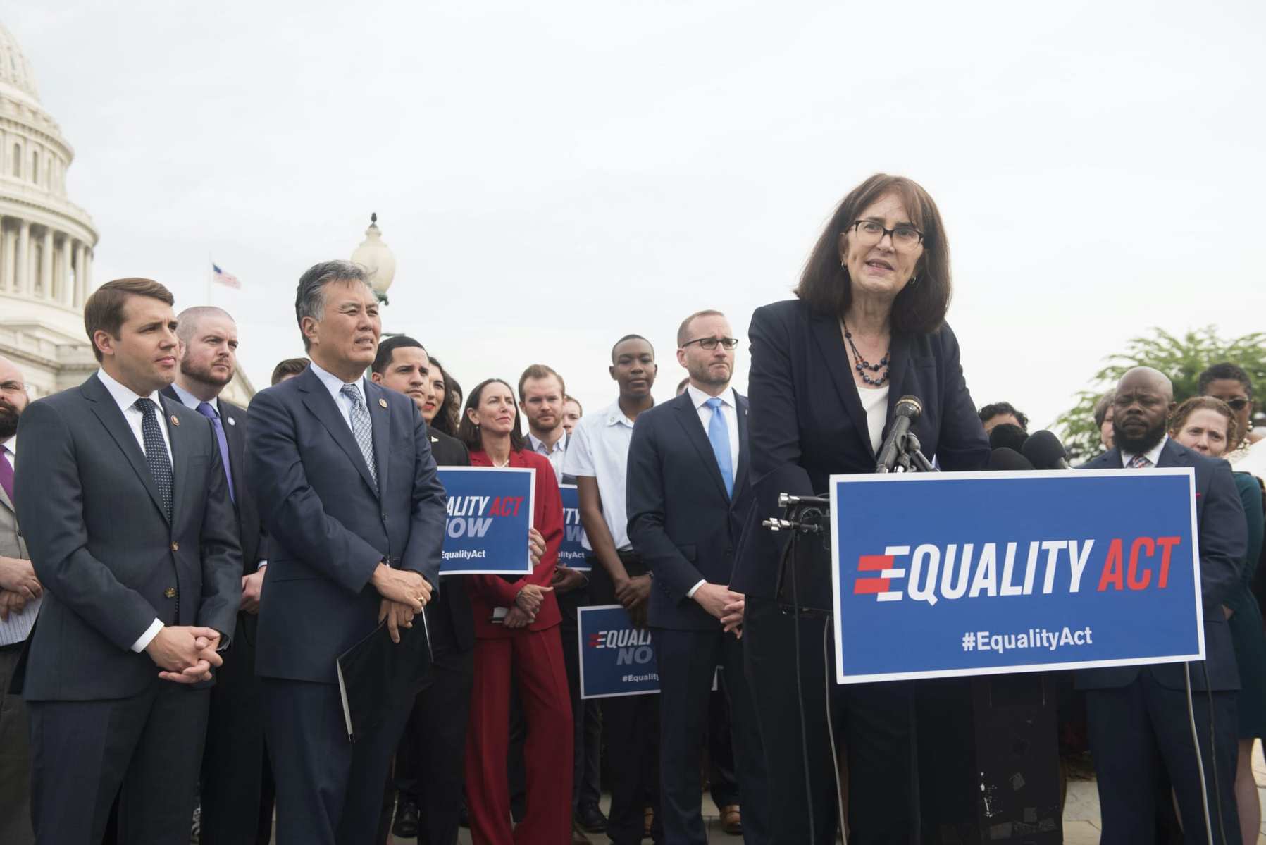 Mara Keisling stands at a podium with a crowd gathered behind her.