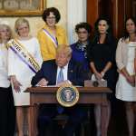 President Donald Trump signs a document surrounded by women surrogates.