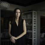 A woman stands in a living room wearing all black.