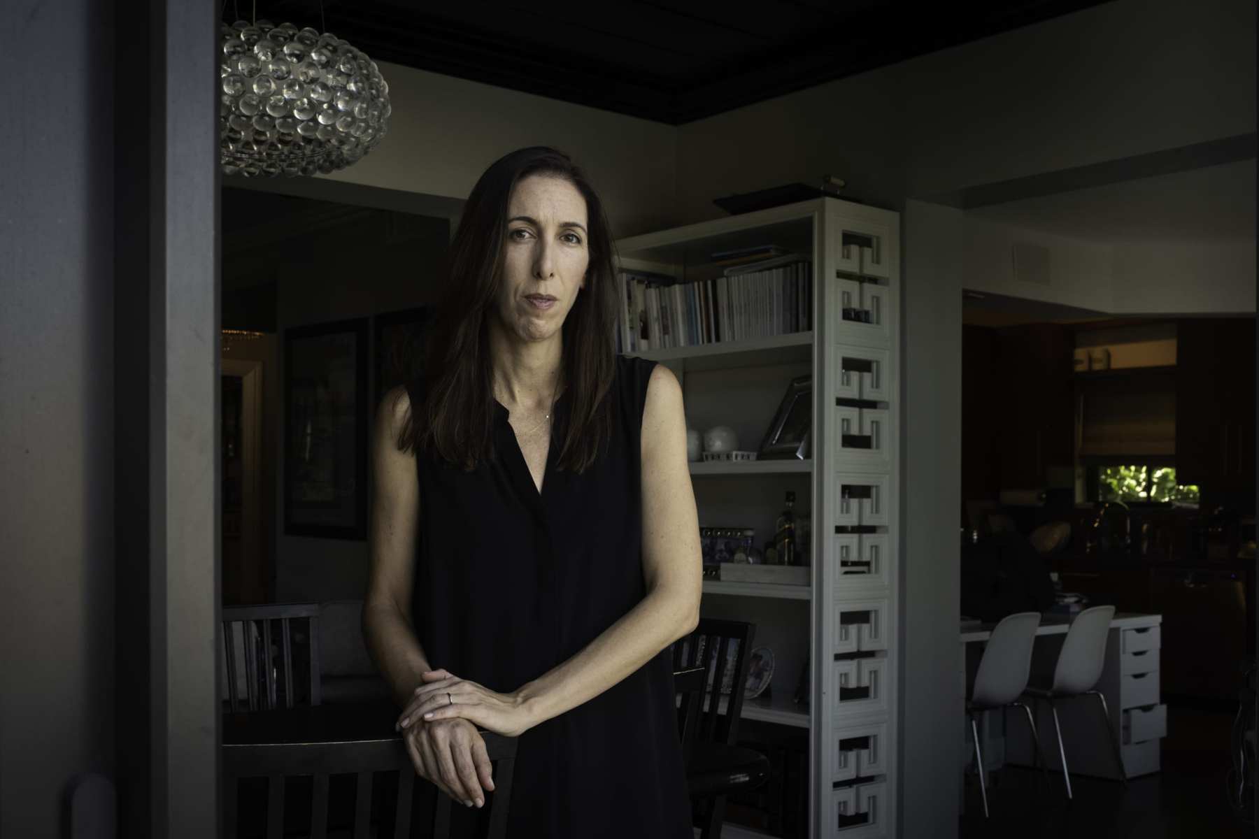 A woman stands in a living room wearing all black.