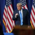 Donald Trump standing in front of a row of American flags.