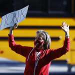 Lara Center, dressed in a red hoodie and holding a sign that says HONK in all caps above her head, protests in Denver to protect public schools from budget cuts.