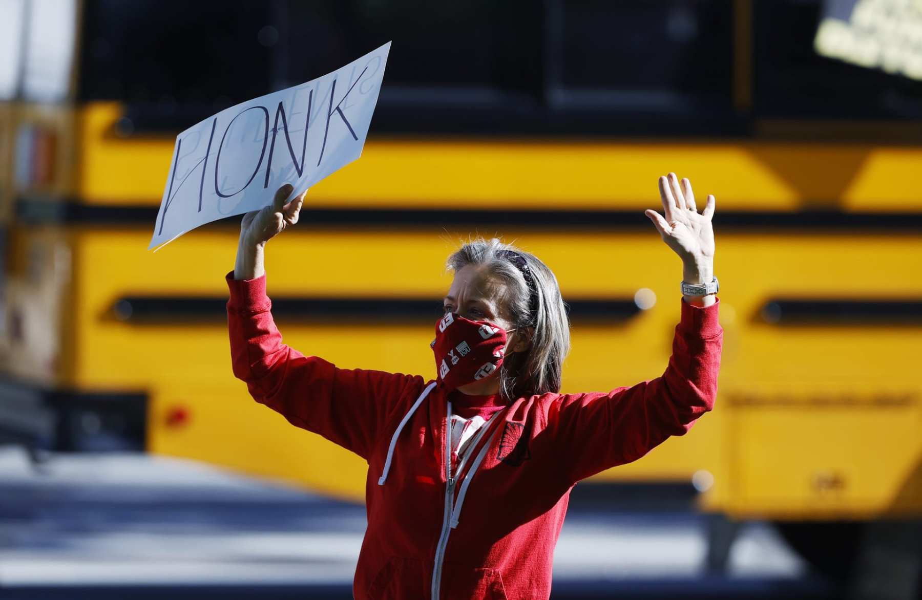 Lara Center, dressed in a red hoodie and holding a sign that says HONK in all caps above her head, protests in Denver to protect public schools from budget cuts.