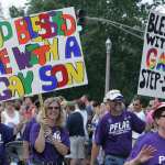 A group of people march with signs supporting their LGBTQ+ children.