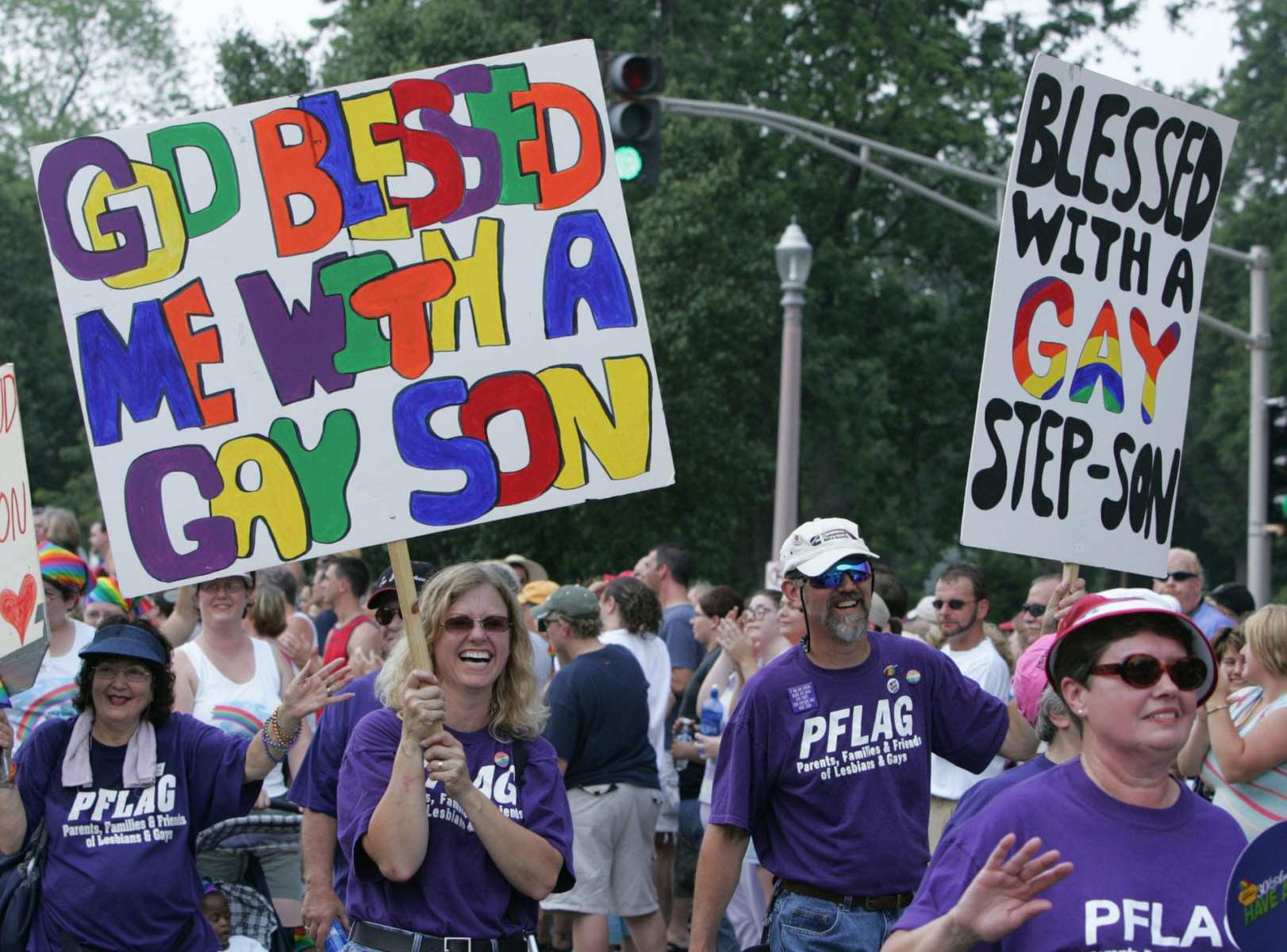 A group of people march with signs supporting their LGBTQ+ children.