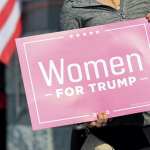 A voter holds a sign in support of Women For Trump outside the Hamilton County Board of Elections as people arrive to participate in early voting, Tuesday, Oct. 6, 2020, in Norwood, Ohio.