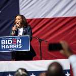 Kamala Harris stands at a podium at a campaign event with a giant Texas flag behind her.