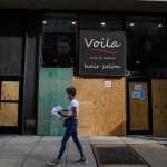 A woman walks by a boarded up business.