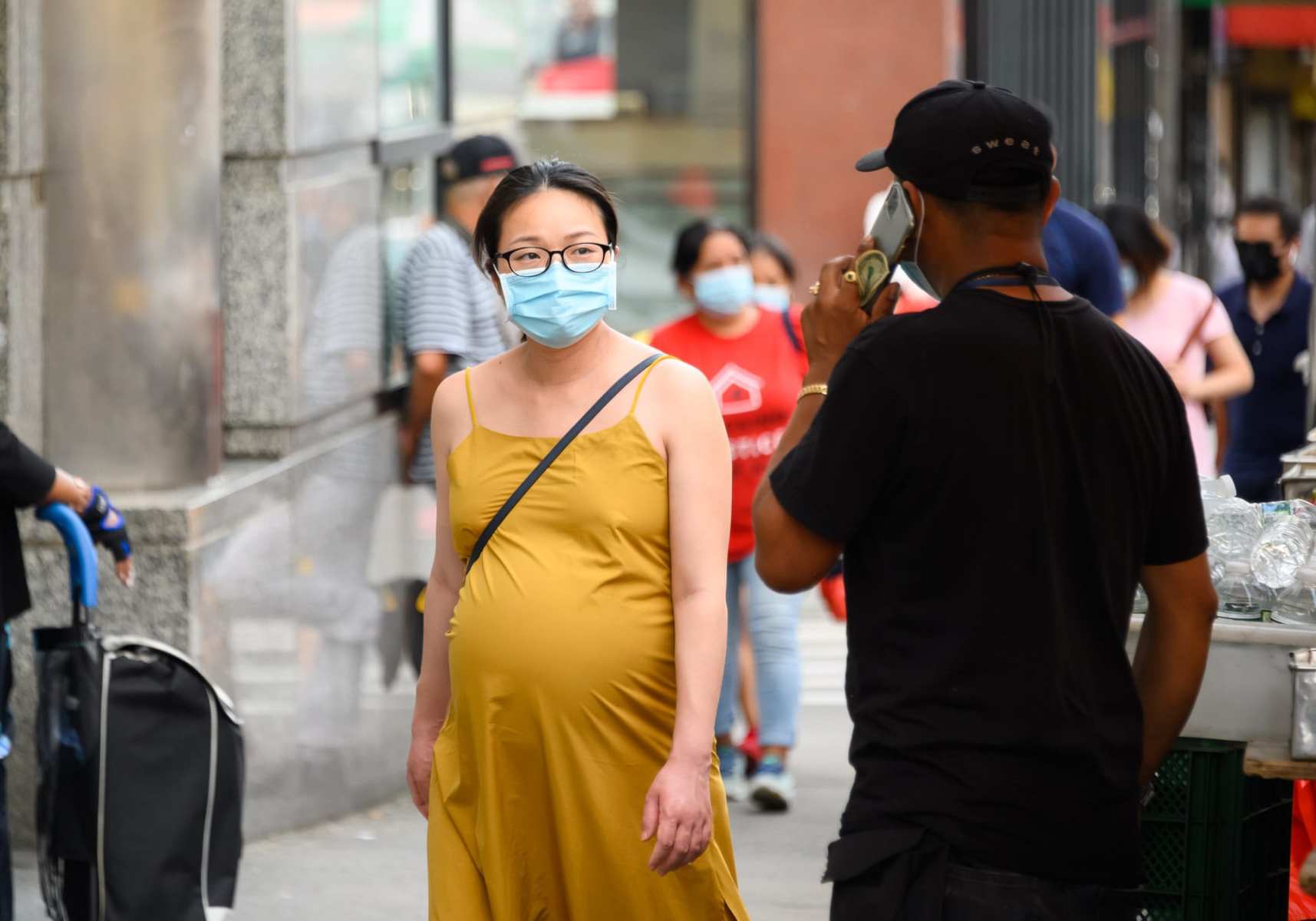 A pregnant woman wearing a face mask walks down the street.