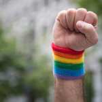 A fist raised in the air with a rainbow cuff.