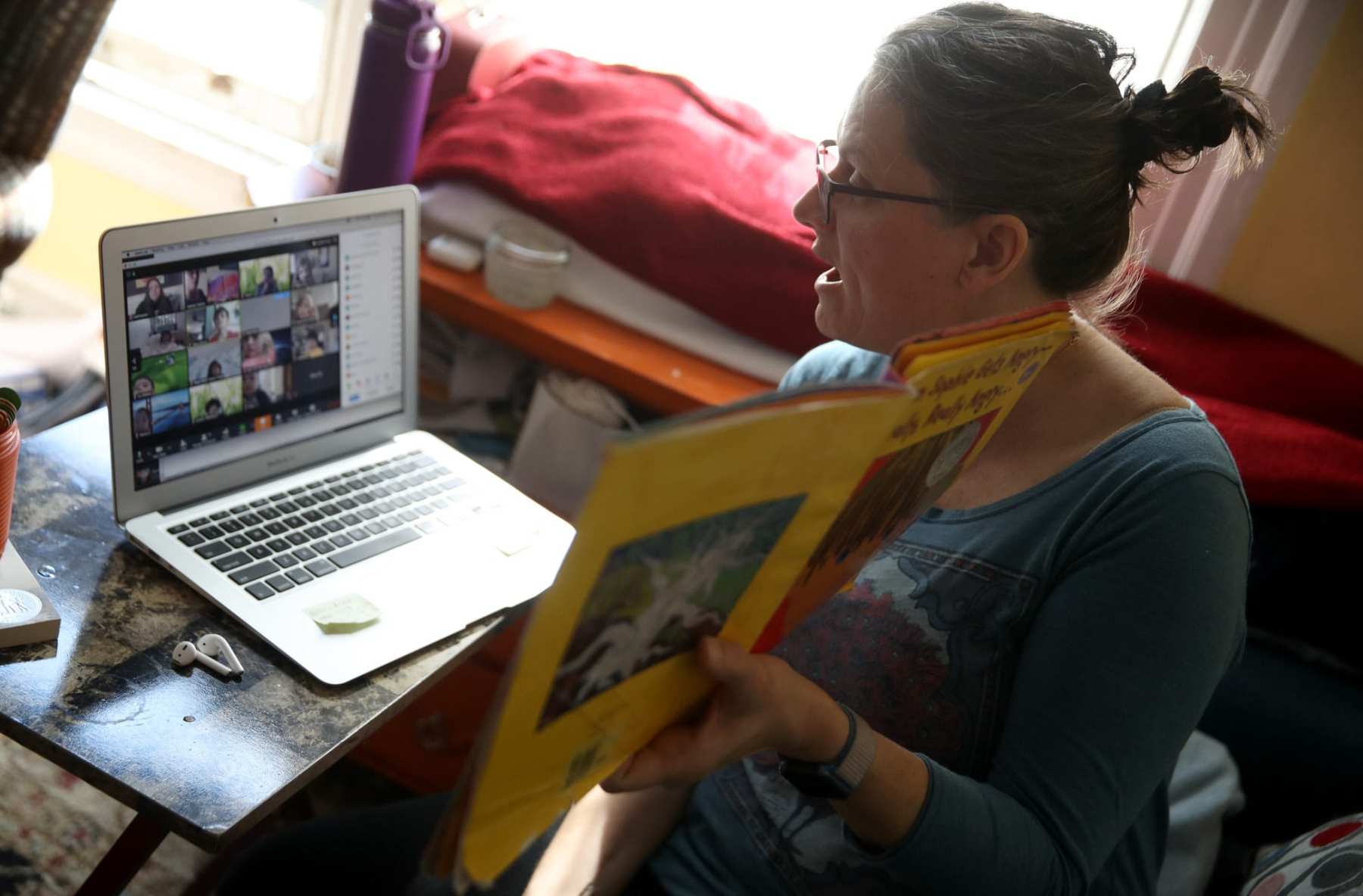 A teacher holding a book in front of the a virtual class.