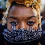 A woman wearing a bandana with BLM painted on her cheeks.