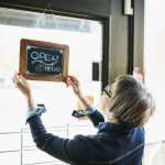 Senior female business owner turning open sign on door before opening boutique