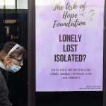 A woman wearing a mask walks past a sign that reads 