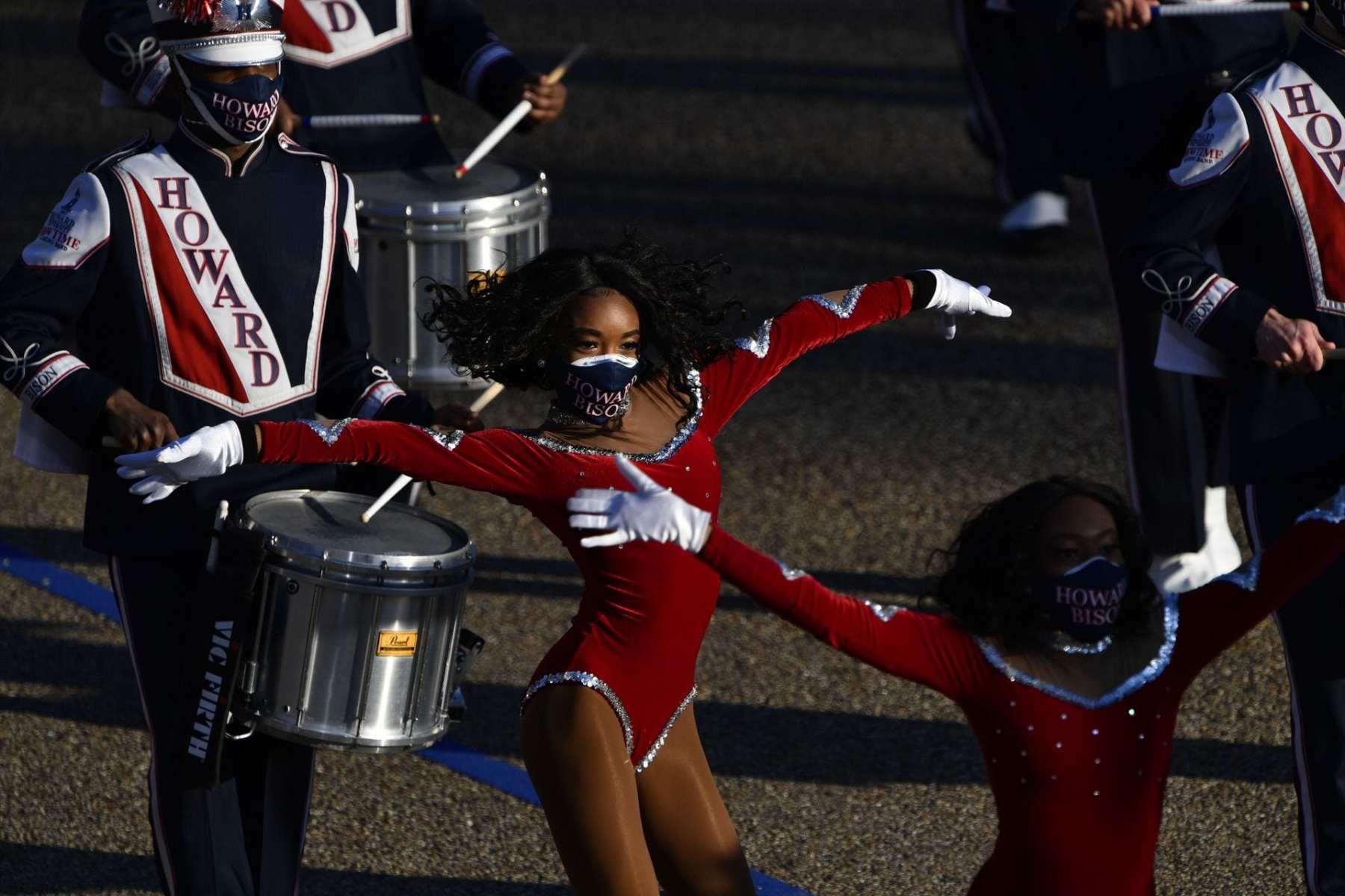 Dancers in red leotards in front of a line of drummers.