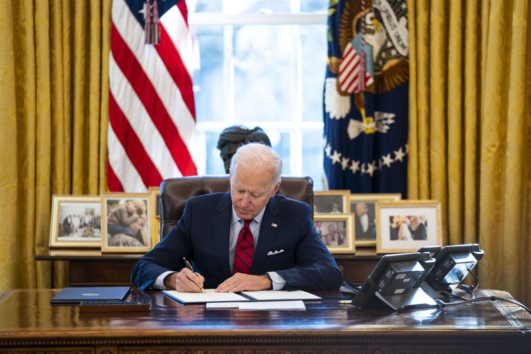 U.S. President Joe Biden signs a series of executive actions at his desk.