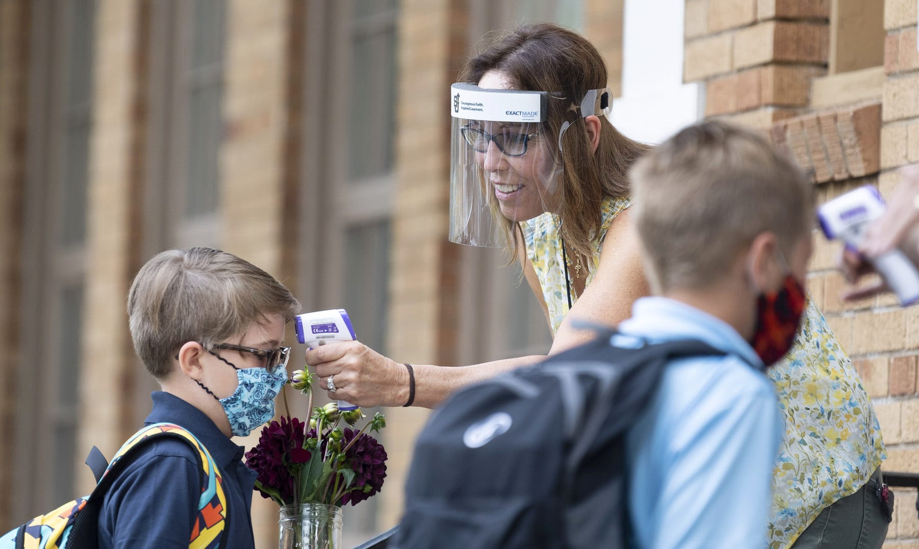 A student wearing a mask has his temperature checked as he enters a school.