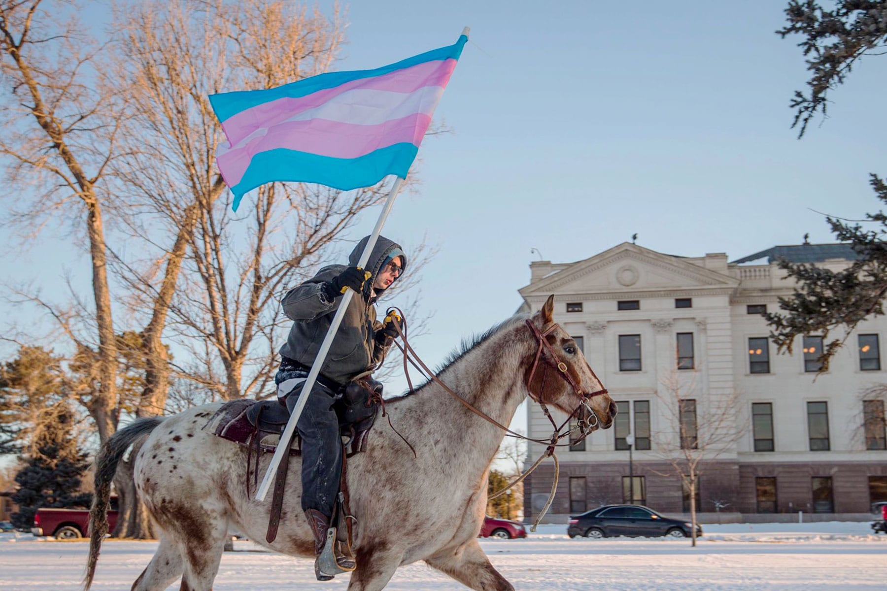 A person rides past the South Dakota Capitol with a trans flag.