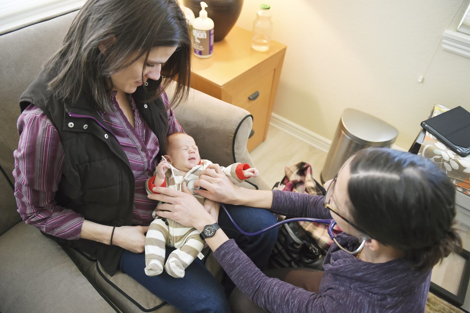 Midwife Lo Kawulok listens to the heartbeat of four week old Solene while her mother Summer Milacek holds her.