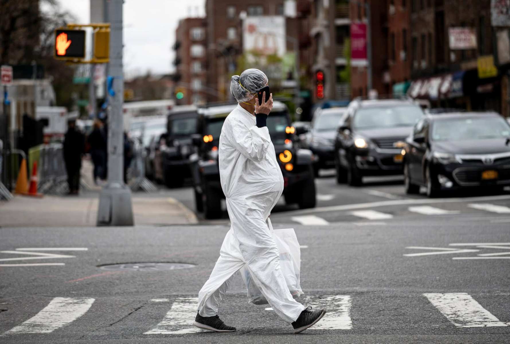 pregnant woman wearing a hazmat suit and a mask walks in the streets in the Elmhurst neighbourhood.