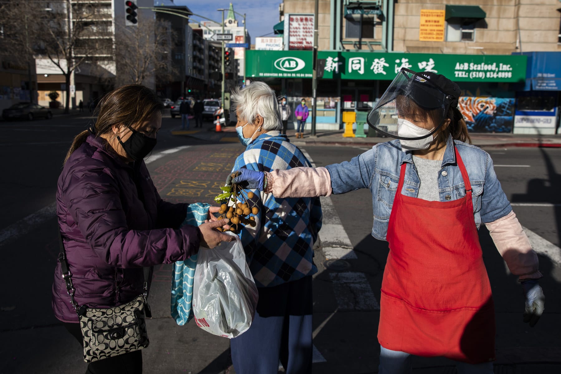 A grocery worker, right, passes a bundle of fresh longan to a woman.