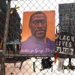 A illustration of George Floyd hangs on fencing next to a sign that reads 