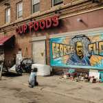 A woman pays respect to a mural of George Floyd by the Cup Foods storefront.