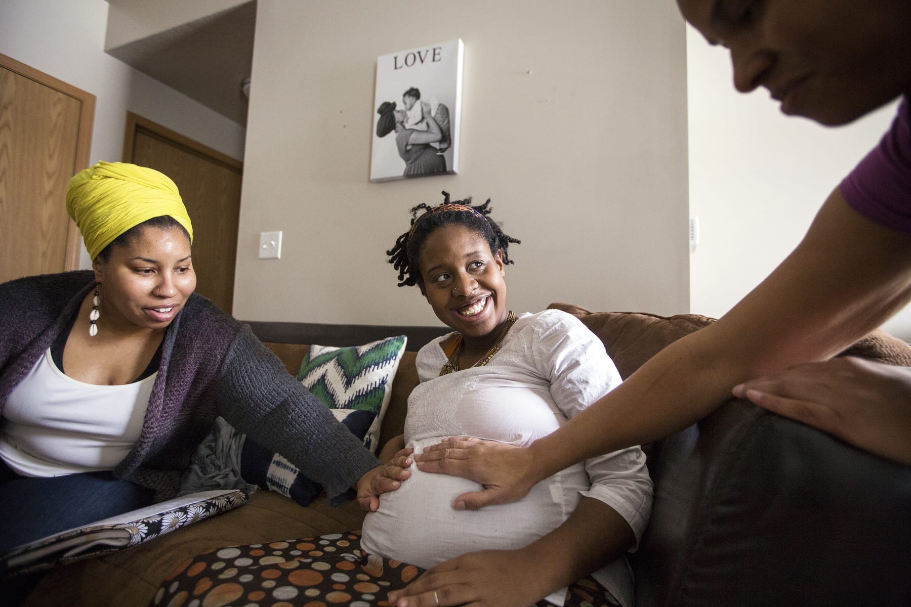 Two midwives tend an expectant mother on her couch.