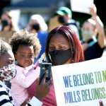 Skyler Mills, 10, left, Kinsey Mills, 2, and their mother Robin Mills, a Mills College alumna, hold up a sign during a rally at Mills College.