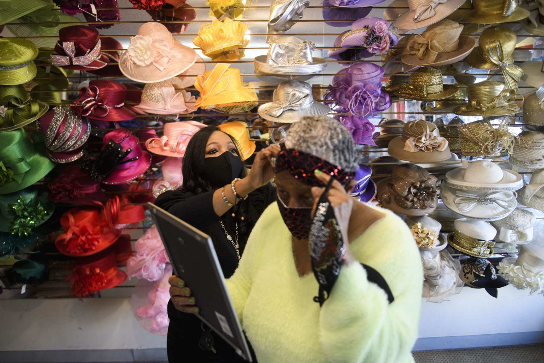 Woman helping another woman try on hats