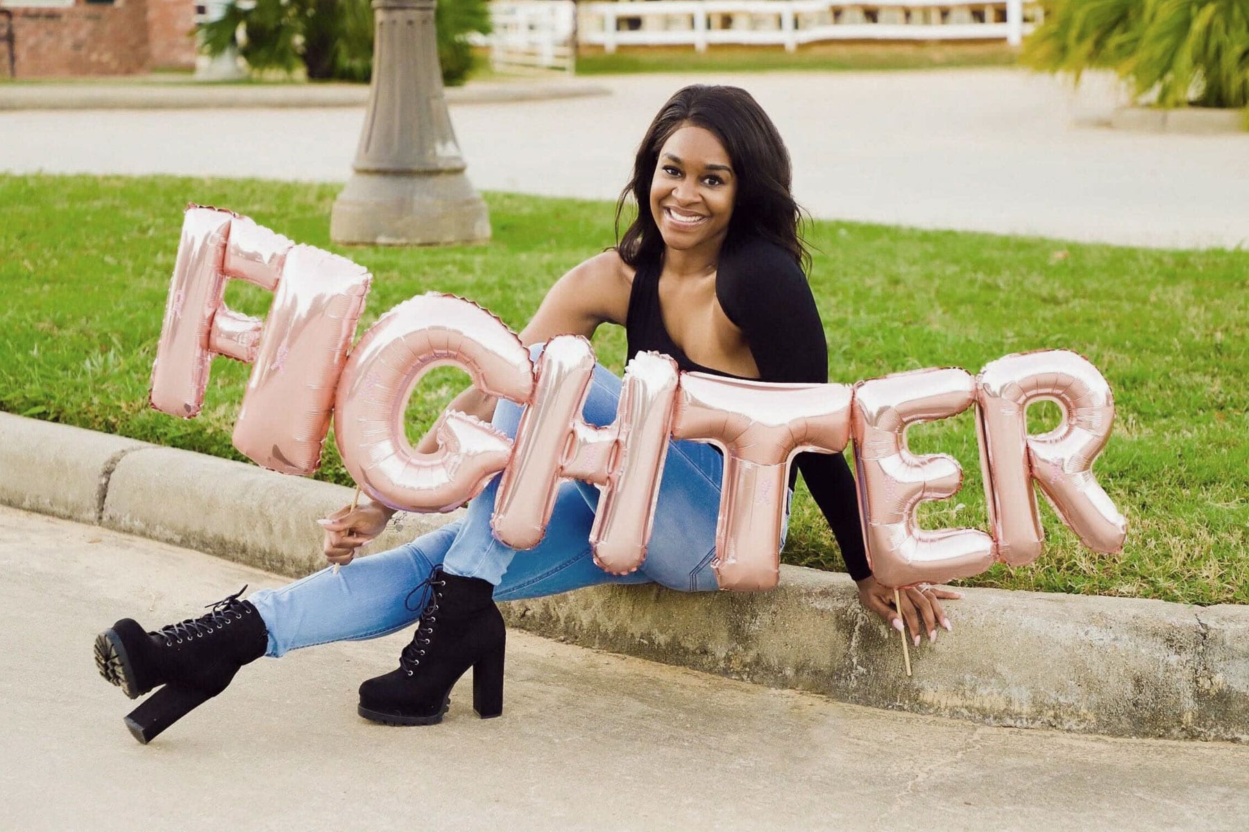 A woman sits on the ground holding a ballon that reads "fighter".