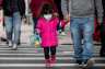 A small girl wearing a mask walks down the street in New York City.