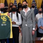 President Biden holding a basketball jersey standing by members of the Seattle Storm.