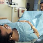 A genderqueer person in a hospital gown receiving a pelvic exam.