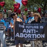 Anti-abortion protesters outside of the Texas Capitol with a sign that reads, 