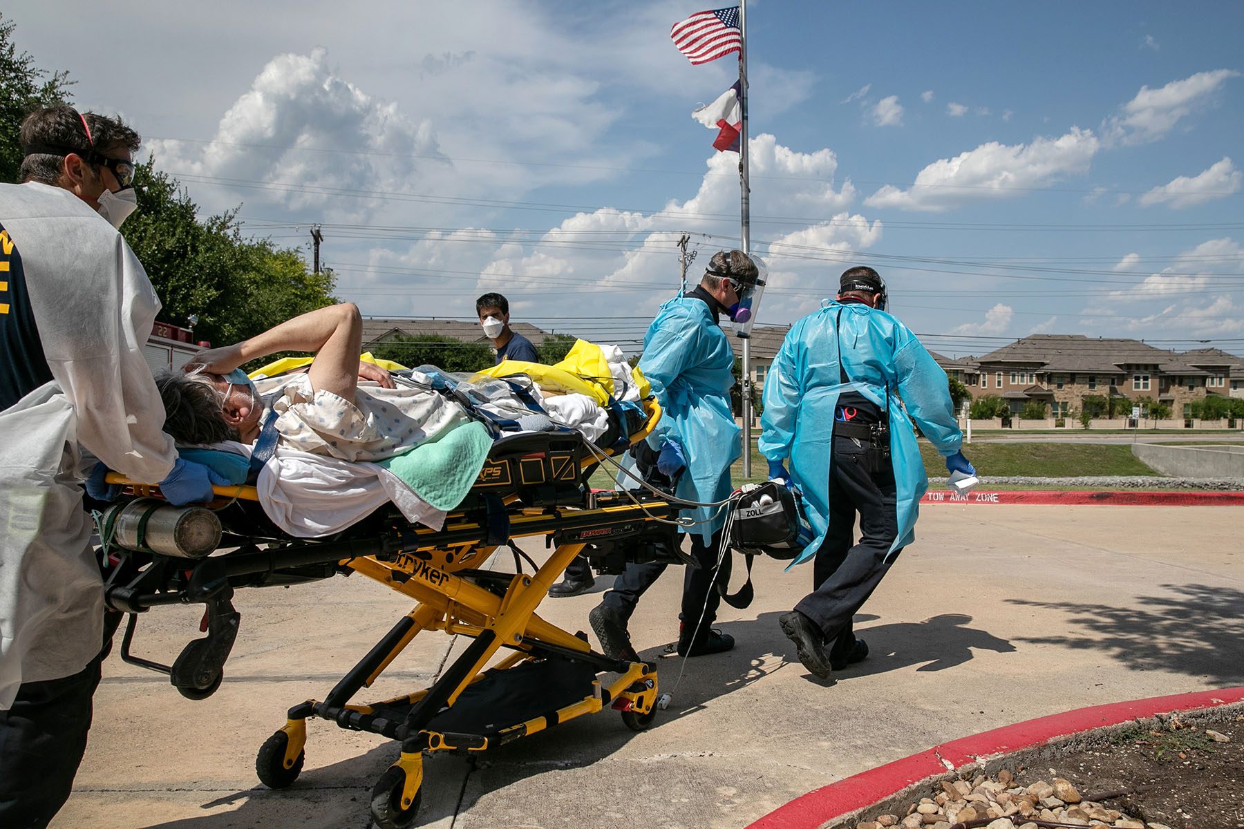 First responders wearing PPE transport a man on a stretcher while he covers his face.