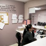 A receptionist is seen answer a phone behind a desk.