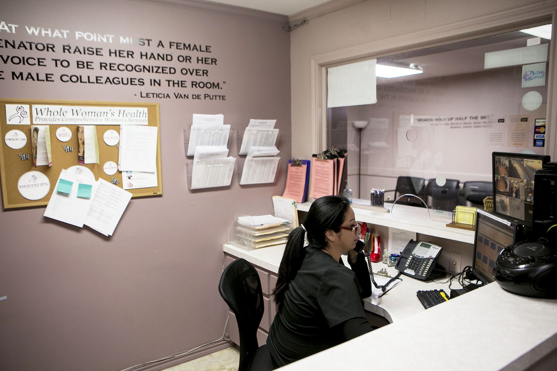 A receptionist is seen answer a phone behind a desk.