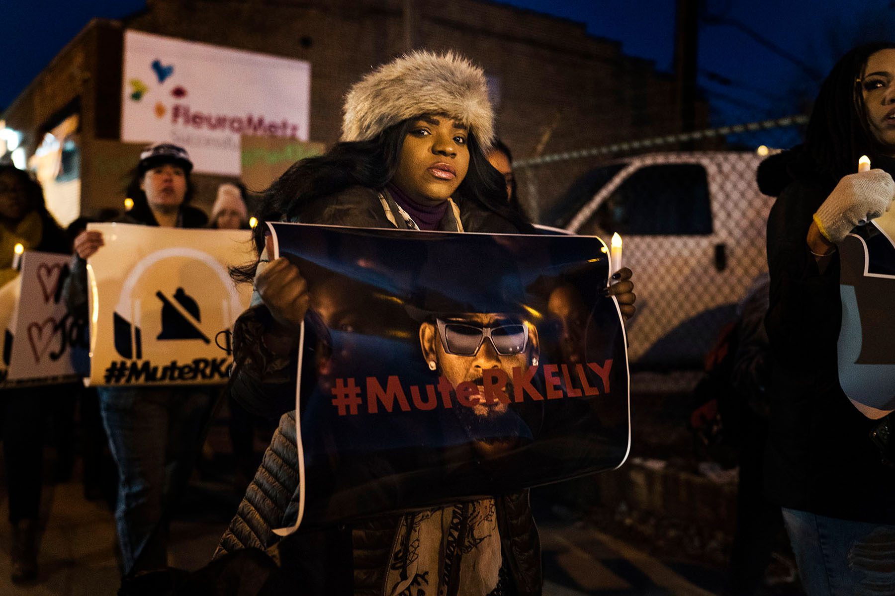 A black woman holds a sign with a picture of R. Kelly with the word #MuteRKelly printed over his face during a demonstration in support of the singer's victims.