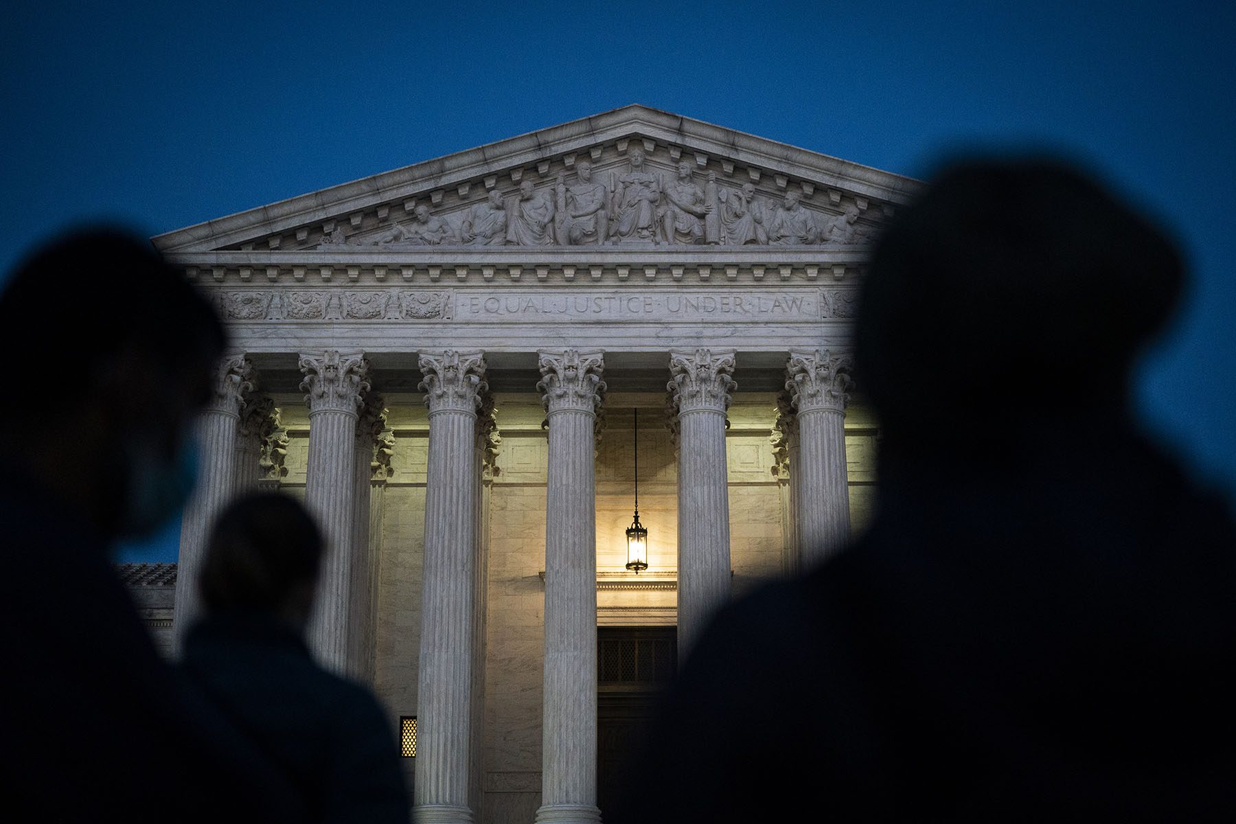 Shadowy figures are seem standing in front of the U.S. Supreme court.