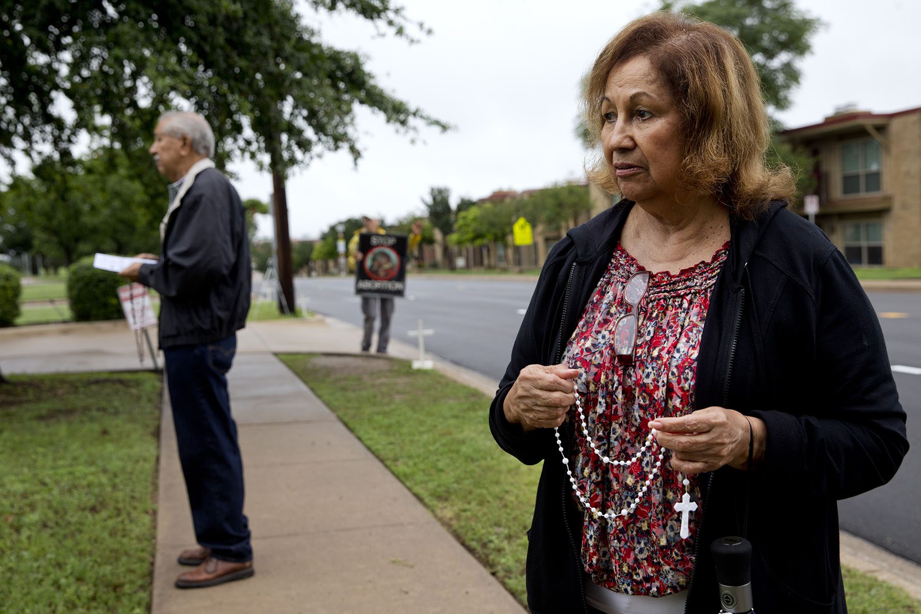 A woman holding a rosary prays outside an abortion clinic.