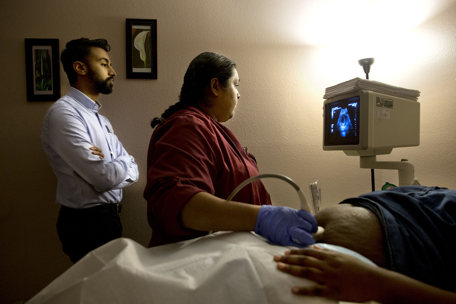 A doctor and a sonographer perform a sonogram on a pregnant patient inside an examination room.