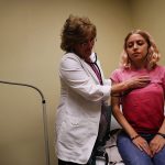 A woman is examined by a nurse in an examination room.