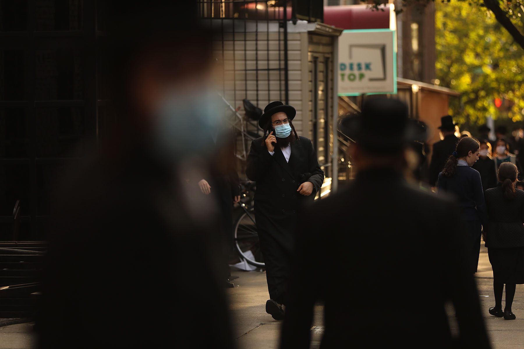 Hasidic people walk along the street, speak on the phone and congregate outside a synagogue.