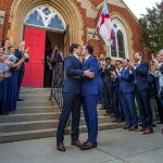 Pete Buttigieg and Chasten Glezman kiss in front of a cathedral while wedding-goers smile and clap.