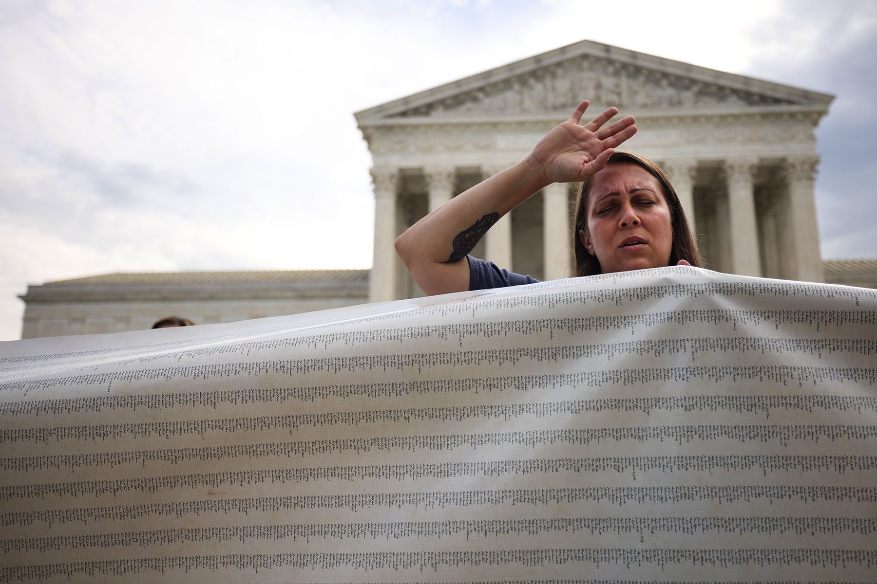 A protester waves her arm into the sky and closes her eyes while holding a large banner in front of the U.S. Supreme Court.